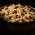 Small bowl of a creamy salad with red pepper, pictured beside the Caesar salad on the menu board